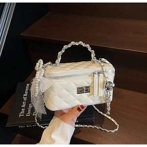 Detail of white quilted crossbody bag with pearl charms and lace bow on a wooden surface
