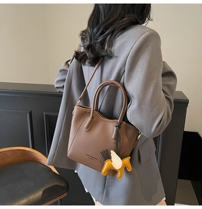 Detail of brown lychee texture leather tote bag with yellow horse charm and brand logo