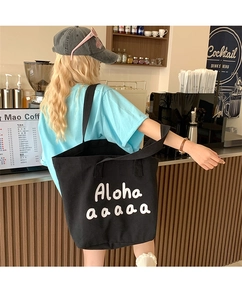 Close-up of a black canvas tote bag with white graffiti lettering and wide shoulder strap
