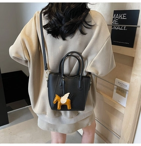 Detail of black lychee leather bucket bag with yellow pegasus charm on beige knit sweater