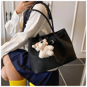 Detail of black woven leather tote bag with a cute white plush bear charm accessory