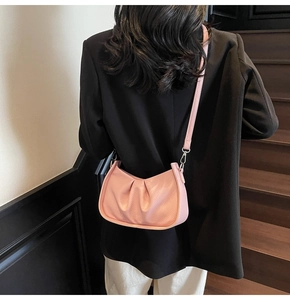 Detail of pink pleated half-moon shoulder bag with silver metal buckle on model