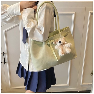 Detail of green woven tote bag with buckle strap and cute plush bear charm