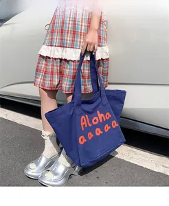 Detail of blue canvas tote bag featuring orange Aloha text and reinforced handle straps