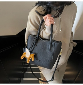Detail of black lychee grain leather tote bag with a colorful horse charm pendant