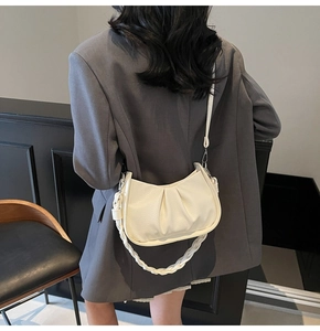 Detail of a creamy white pleated hobo bag with braided handle and adjustable strap