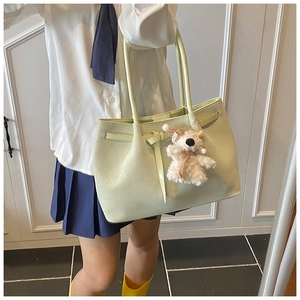 Detail of light green tote bag with woven texture, bow decor, and cute bear pendant