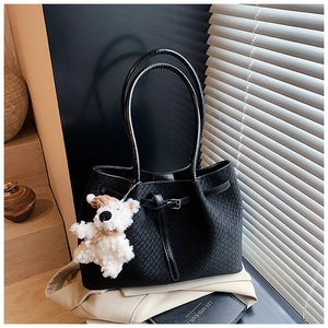 Black woven tote bag with silver buckle and cute teddy bear charm on beige trench coat