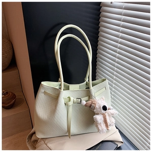 Detail of mint green woven tote bag with a small plush bear charm in soft natural light