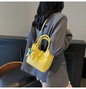 Détail du sac seau en cuir jaune à texture litchi avec breloque cheval sur mannequin