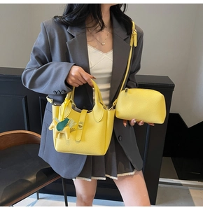Détail du sac seau jaune à texture litchi avec breloque cheval sur blazer gris chic