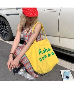 Detail of a large yellow canvas tote bag with green Aloha lettering in a casual outdoor setting