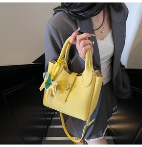 Détail du sac seau jaune en cuir grainé avec breloque cheval porté sur un tailleur gris