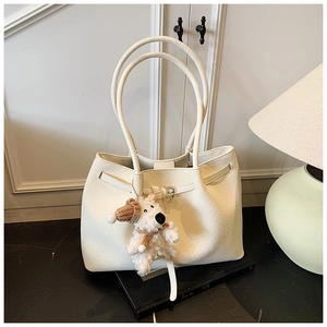 Detail of white tote bag featuring woven texture and a cute plush puppy charm accessory