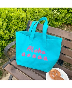 Detailed close-up of a blue canvas tote bag with pink Aloha printing on a wooden bench