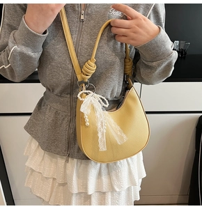 Dettaglio borsa gialla a mezzaluna con trama litchi, fiocco in pizzo di perle e tracolla