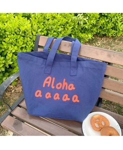 Detail of blue canvas tote bag featuring vibrant orange Aloha print on a park bench