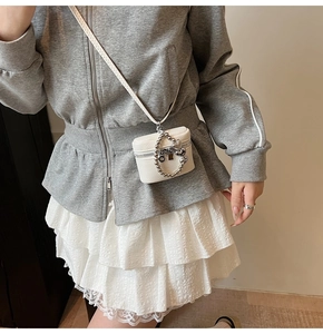 Detail of a white textured leather mini crossbody bag with silver bow charm and bead chain