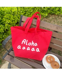 Detail of red canvas tote bag featuring white Aloha script on a wooden bench