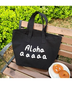 Detail of a large capacity black canvas tote bag with white Aloha print on a park bench