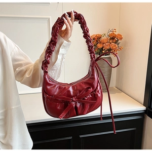 Detail of burgundy crescent bag with pleated handle and 3D bow on polished faux leather