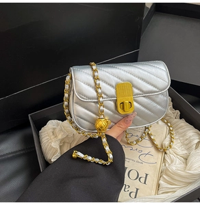 Détail d'un sac argenté matelassé avec chaîne dorée et breloque boule métallique