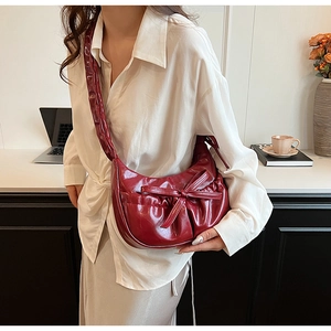 Detail of burgundy ruched crescent bag with large bow and glossy finish on leather