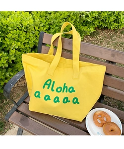 Close-up of bright yellow canvas tote bag with green Aloha print on outdoor wooden bench