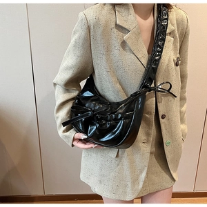 Close-up of black glossy leather crescent bag with side bow detail on beige blazer