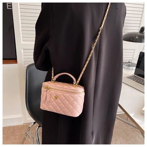 Detailed view of a pink quilted chain bag with gold floral accents on a black coat