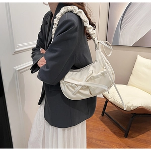 Detail of a creamy white crescent bag with pleated straps and bow decoration worn by a model