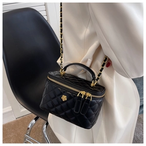 Detail of a black quilted vanity bag featuring a gold camellia charm and chain strap