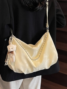 Sac hobo beige chic avec chaîne argentée et pendentif ours porté par un mannequin en style urbain