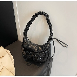 Detail of black glossy faux leather shoulder bag with chic bow and ruched handle