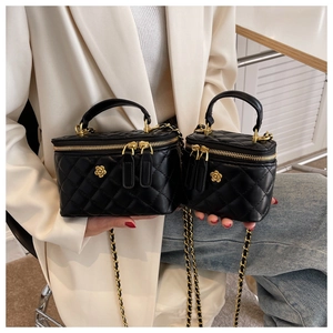 Detail of black quilted leather vanity bags with golden camellia flower and chain strap