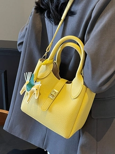 Sac seau en cuir grainé jaune avec breloque cheval sur fond de costume sombre