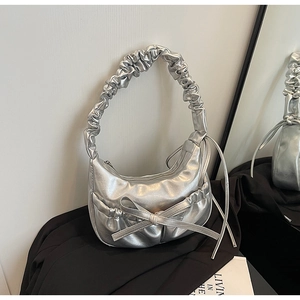 Detail of silver metallic shoulder bag featuring a scrunchie handle and bow decoration