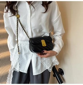 Détail d'un sac bandoulière matelassé noir avec chaîne dorée et boule métallique décorative
