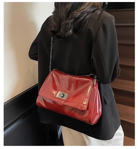 Detail of red glossy patent leather tote bag with silver chain strap on model shoulder