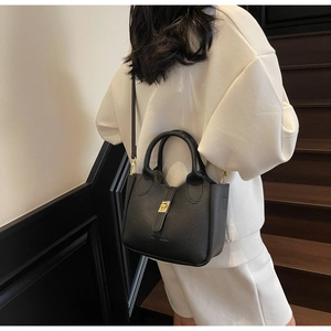 Detail shot of black lychee grain leather bucket bag with golden twist lock on white hoodie