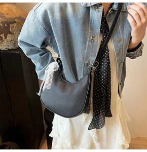 Dettaglio borsa a mezzaluna in pelle nera con fiocco in pizzo bianco su giacca denim