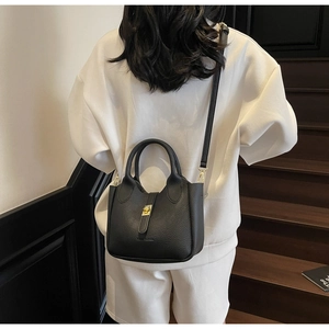 Detail view of black lychee textured leather bucket bag with gold hardware worn by a model