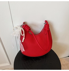 Dettaglio borsa a mezzaluna rossa in pelle litchi con fiocco di pizzo e ciondolo di perla