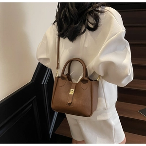 Detailed view of brown litchi pattern leather bucket bag with gold metal clasp on shoulder