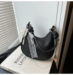 Dettaglio della borsa a mezzaluna in pelle nera con fiocco in pizzo bianco e perle