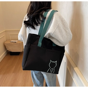 Detail of a black canvas tote bag with a green cat logo and spacious front pocket