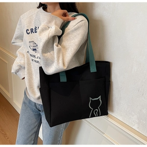 Minimalist black tote bag featuring a contrasting green strap and a small cat embroidery