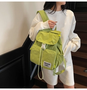 Close-up of avocado green backpack with dual front pockets and woven letter patch
