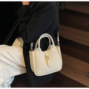 Close-up of beige lychee grain leather bucket bag with gold clasp and shoulder strap