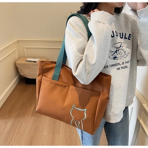Close-up of brown canvas tote with green straps and light blue cat embroidery details
